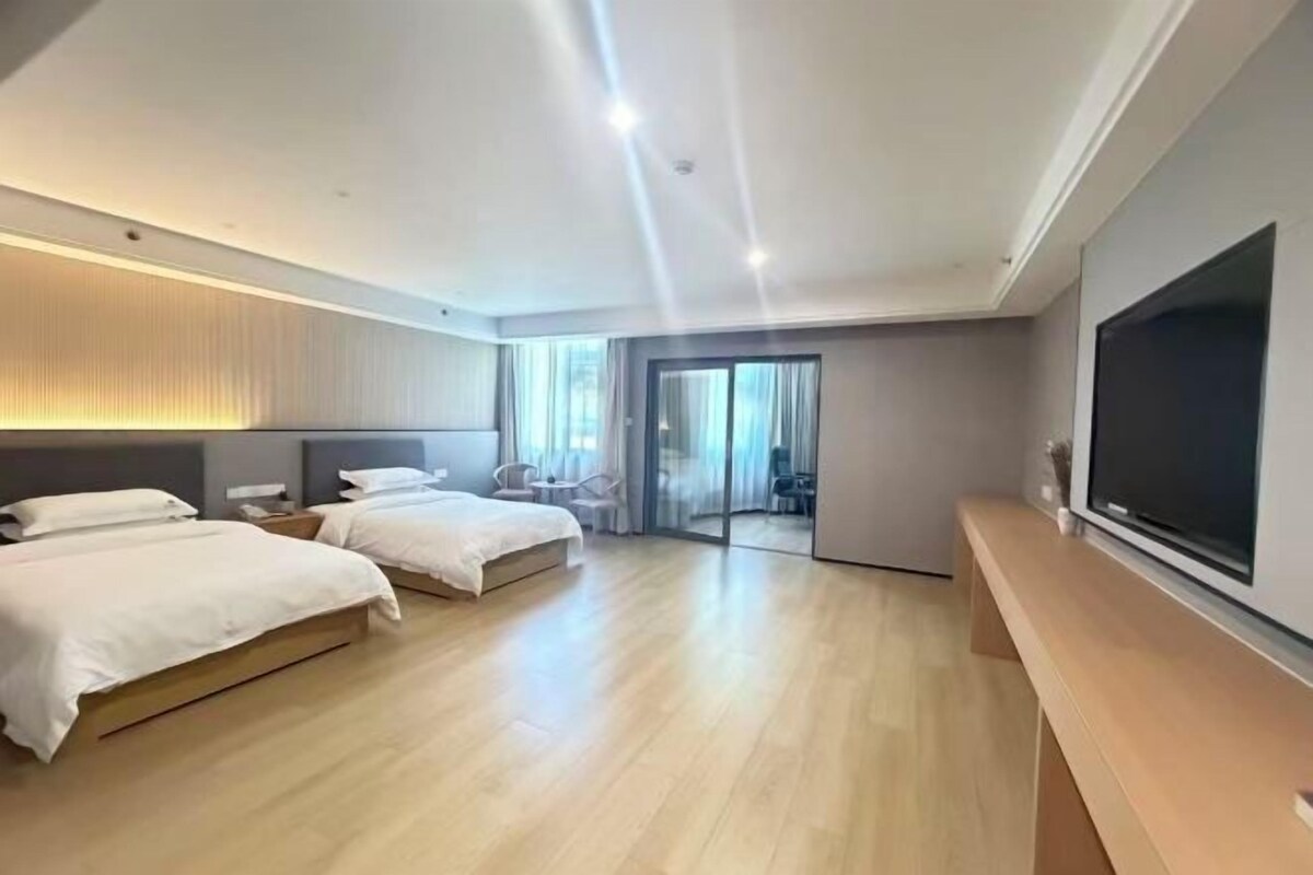 Una habitación de hotel moderna con dos camas, un televisor grande y una puerta corredera que da a un balcón.