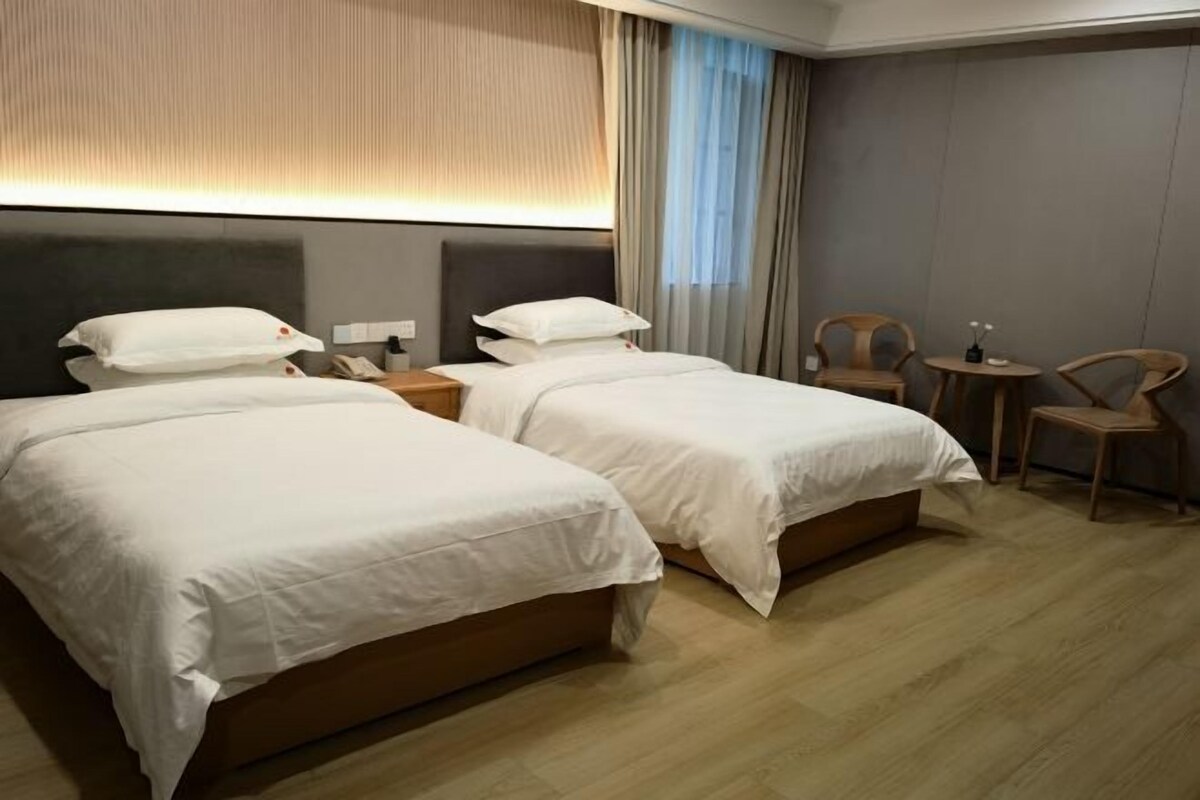 Habitación de hotel con dos camas, una mesita de noche con lámpara, una silla y una pequeña mesa.