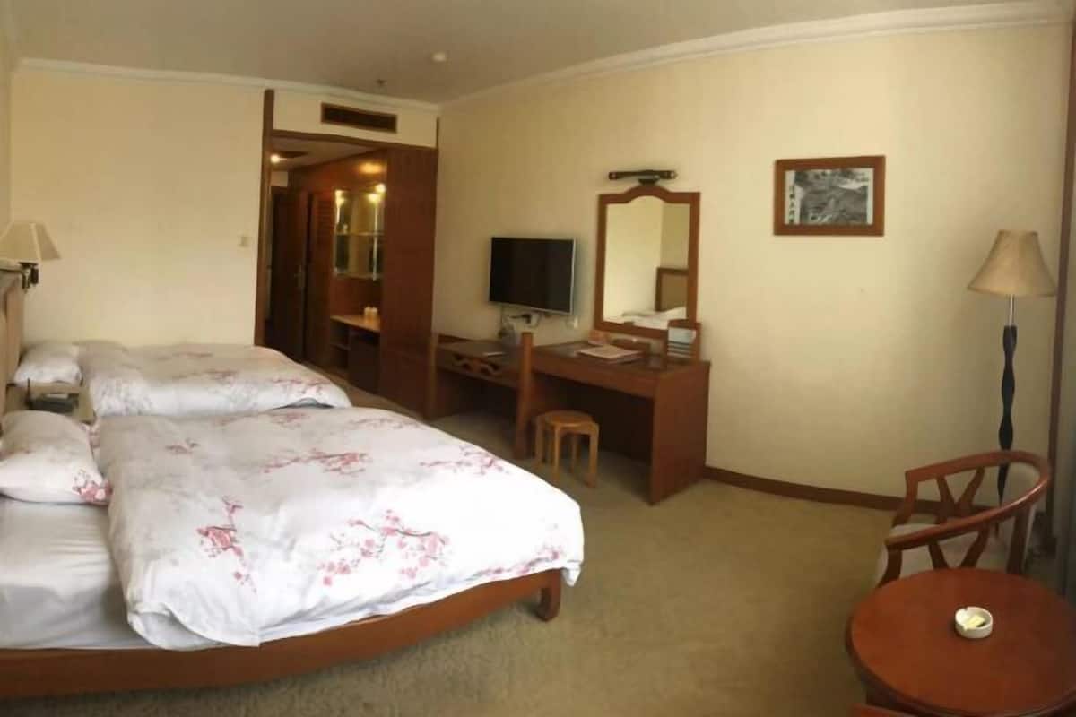A hotel room with a bed, a desk, a chair, a television, and a lamp.