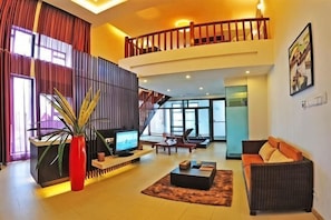A spacious living area with a TV, seating, a staircase, and a balcony.