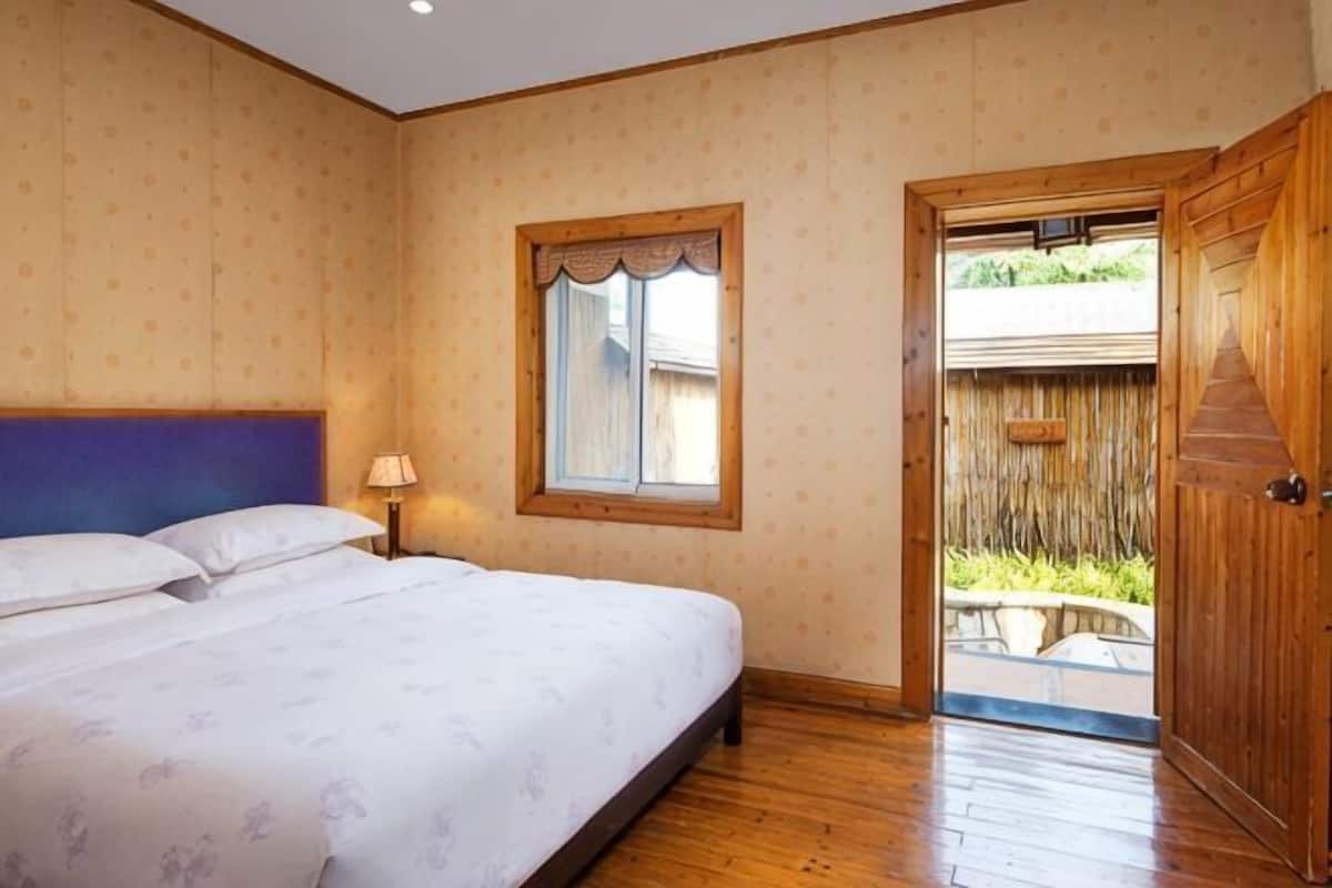 A bedroom with a bed, a window, a door, and a view of the outside.