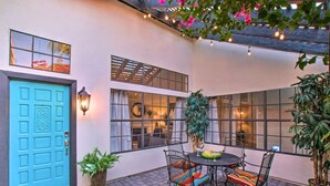 Un espace patio avec une porte bleue, une table entourée de chaises et des plantes en pot.
