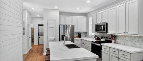 A modern kitchen with white cabinetry, a marble island, stainless steel appliances, and a wooden bar stool seating area.