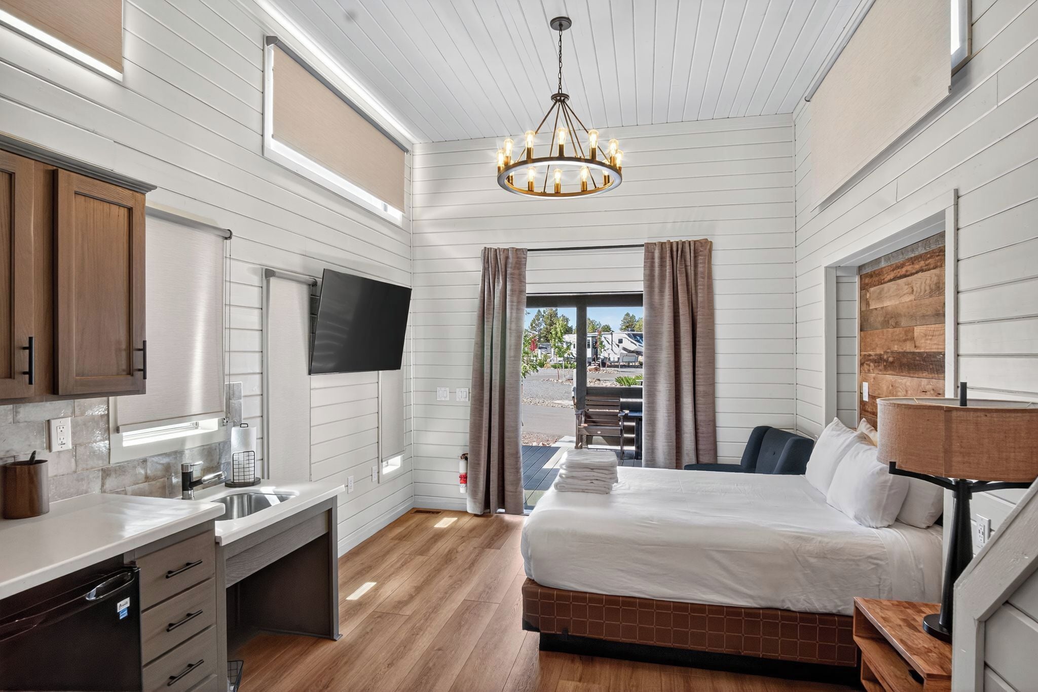 A modern bedroom with a bed, a TV, a desk, and a window with curtains.