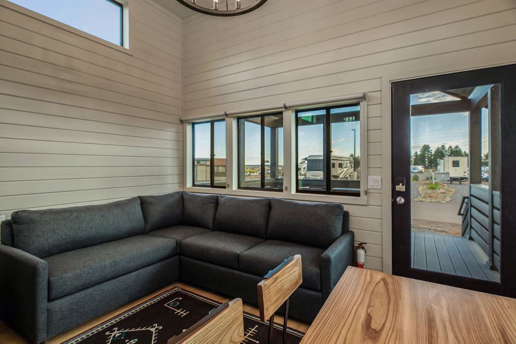 A modern living room with a sectional sofa, a wooden coffee table, and a view through large windows to the outside.