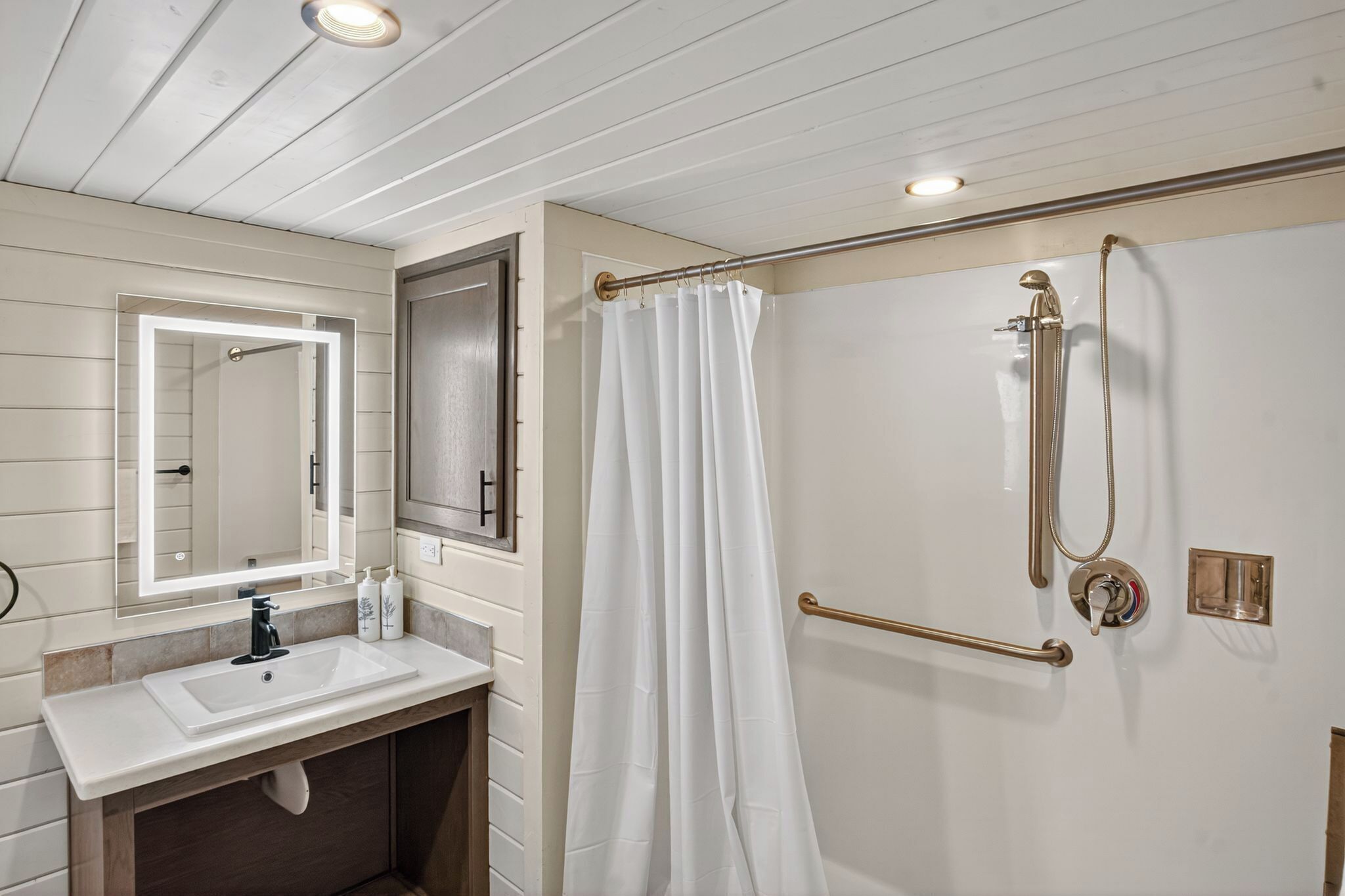A bathroom with a sink, mirror, shower, and grab bars.