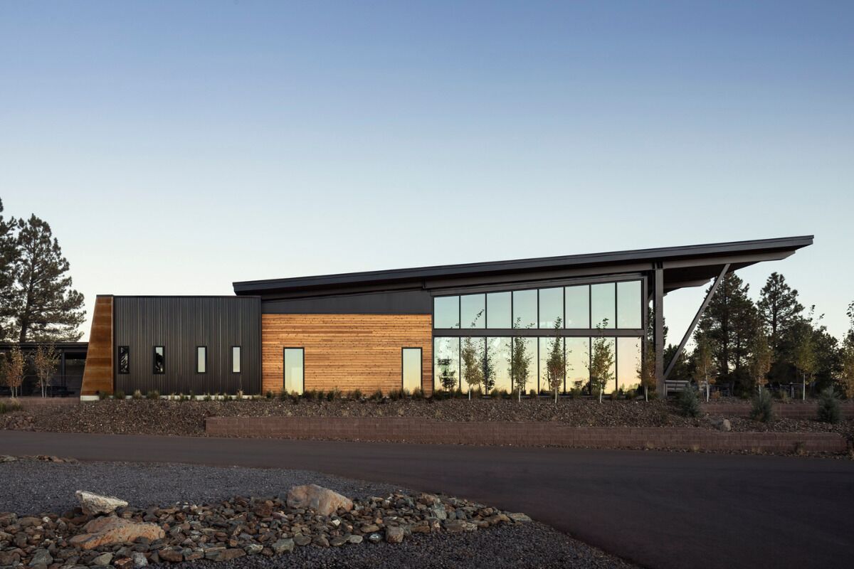 A modern building with a sloped roof, large windows, and a mix of wood and metal materials.