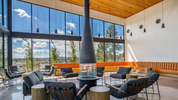 A spacious lounge area with modern furniture, a large fireplace, and large windows offering a view of the outdoors.