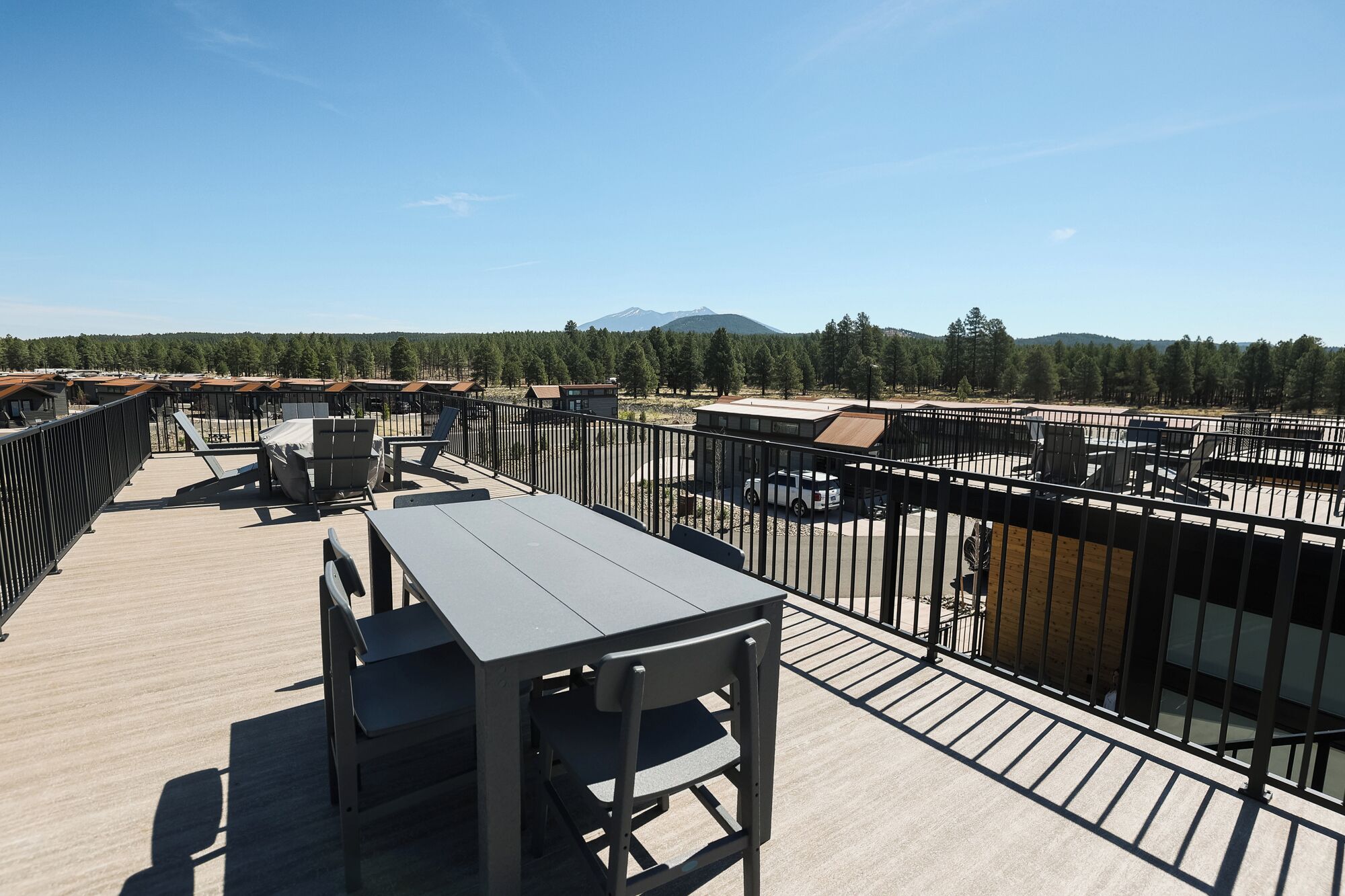 A rooftop terrace with a table and chairs, a view of a forested area, and a distant mountain.