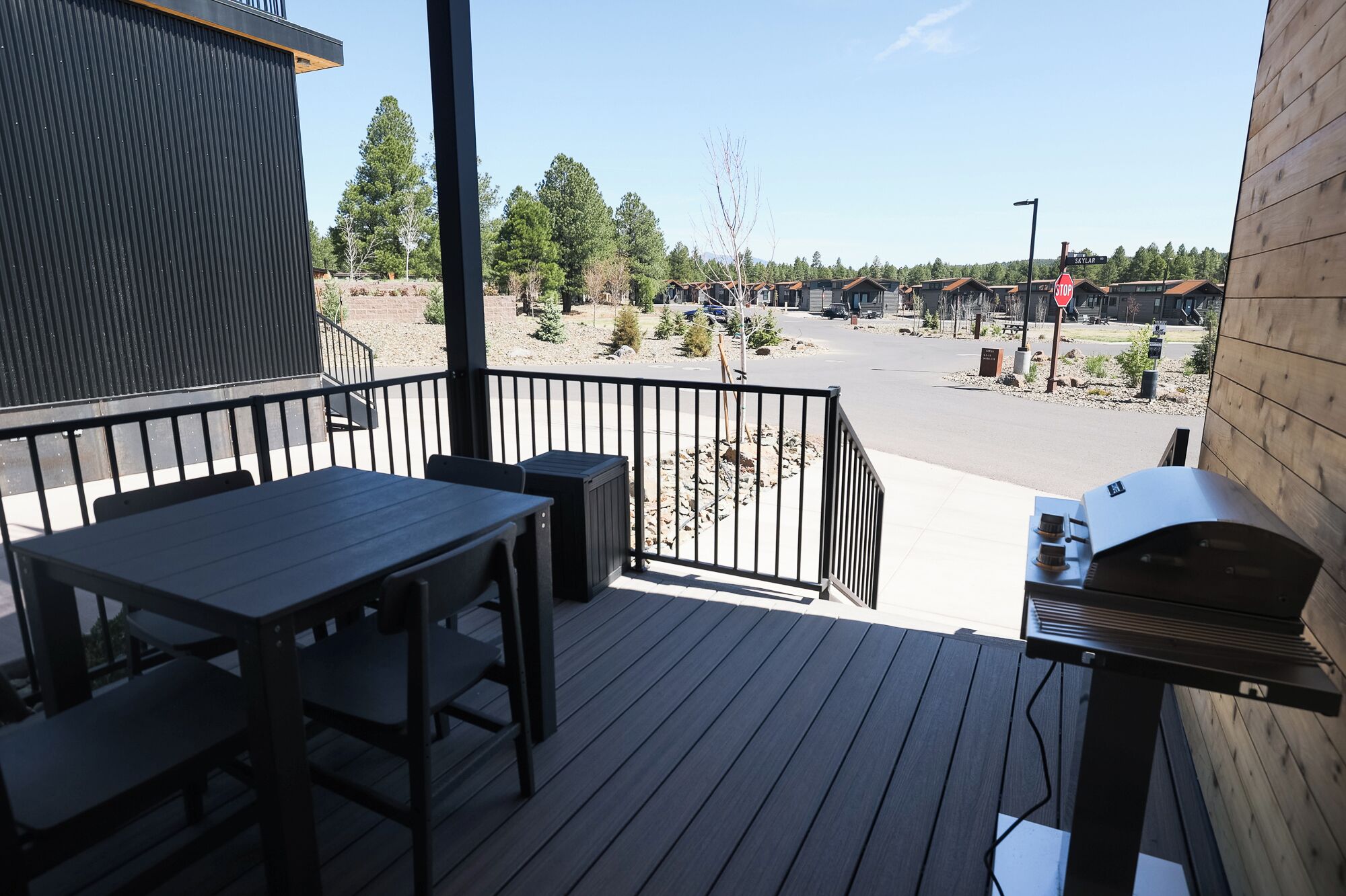 A wooden deck with a grill, a table, and chairs, overlooking a parking area and buildings.