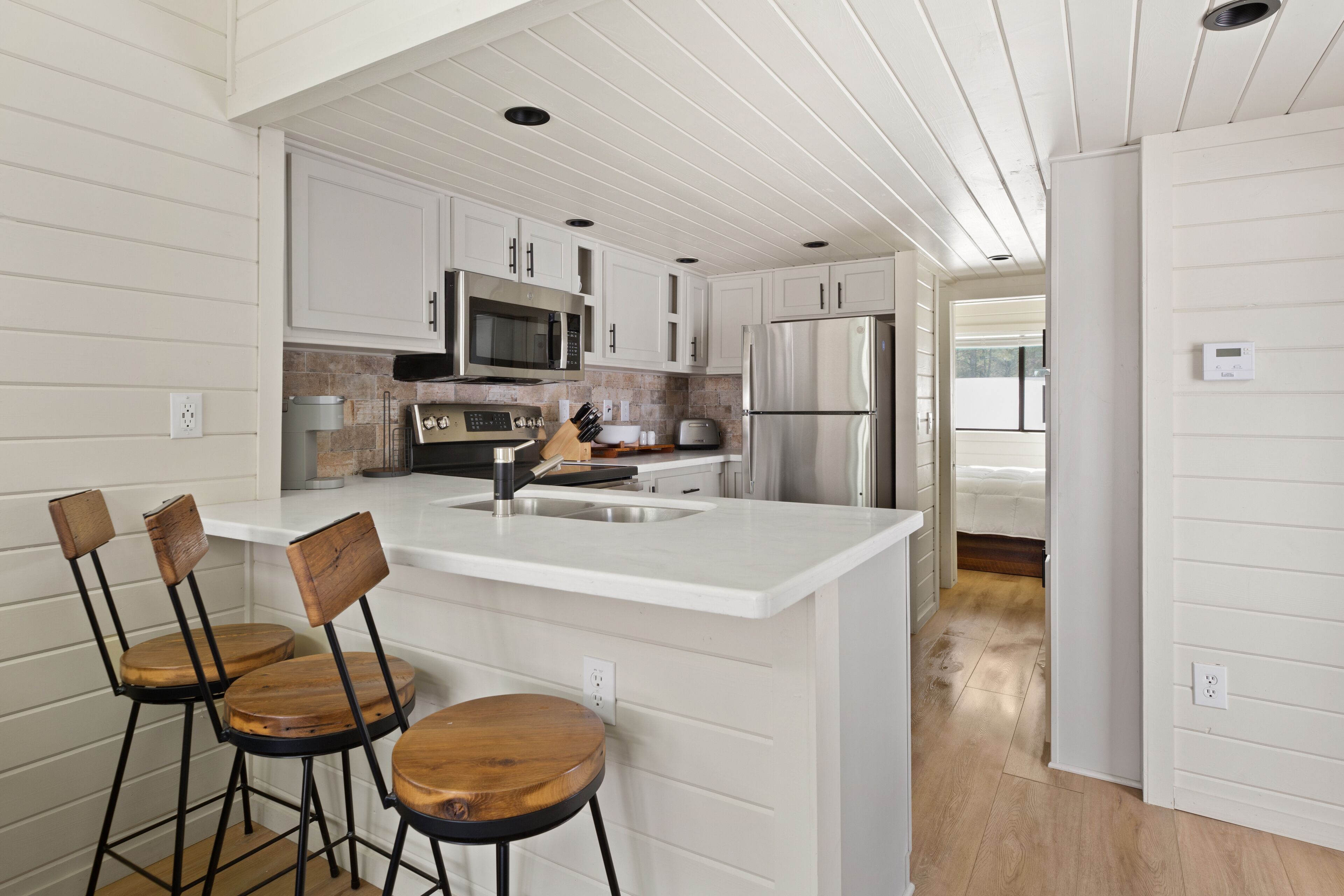 A modern kitchen with white cabinetry, a central island with bar stools, stainless steel appliances, and a visible thermostat.