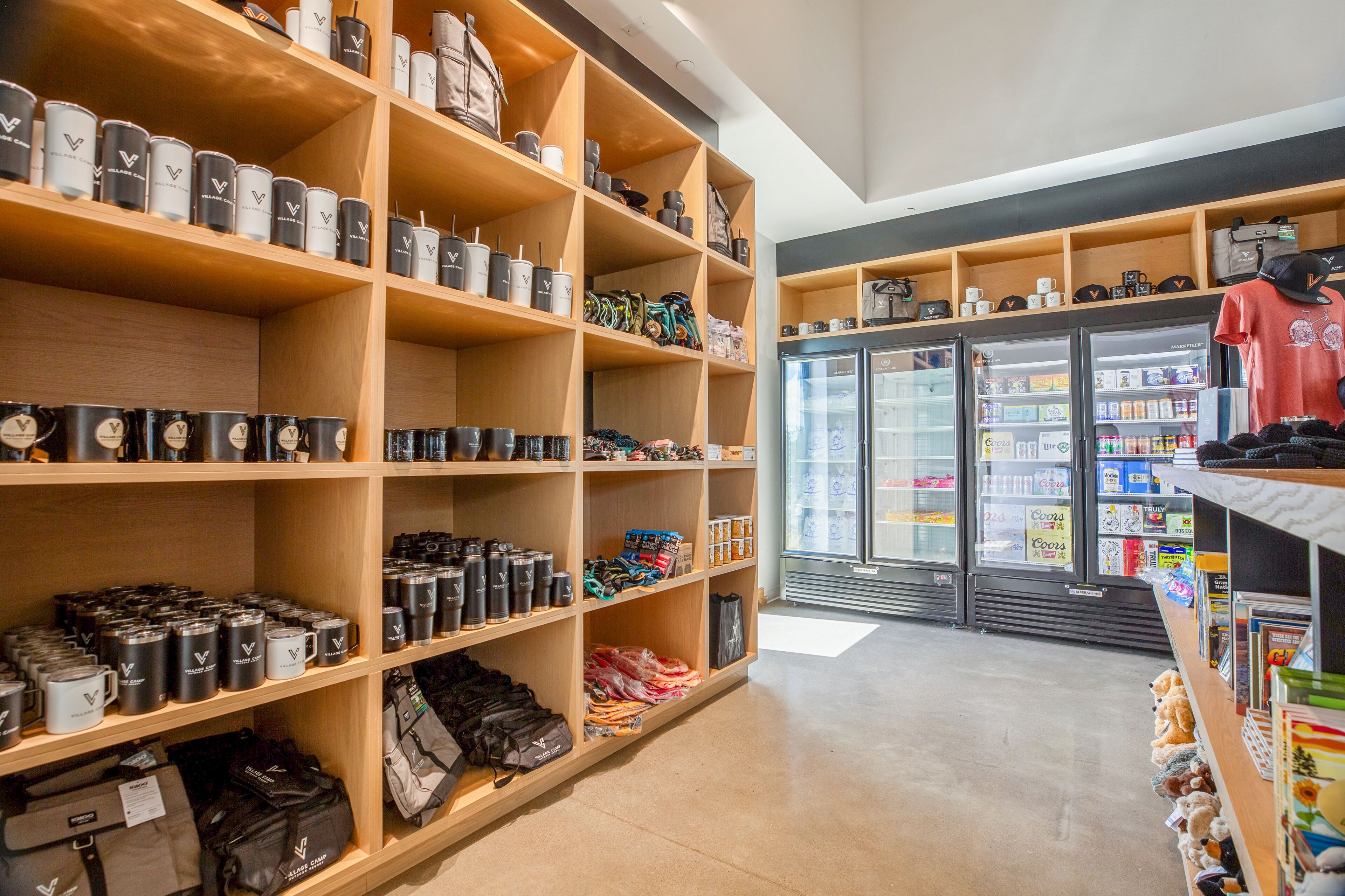 A store with shelves stocked with mugs and bags, a refrigerated display case, and a mannequin in a red shirt.