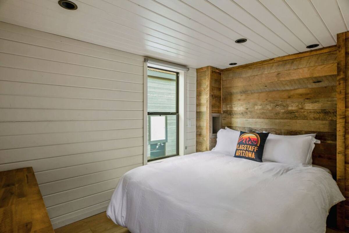 Une chambre à coucher avec un lit, une tête de lit en bois, une fenêtre avec des stores et un banc en bois.