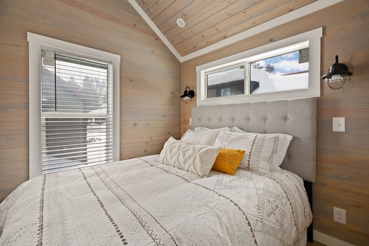 Une chambre avec un grand lit, des murs en bois, une fenêtre avec des stores et un luminaire fixé au mur.