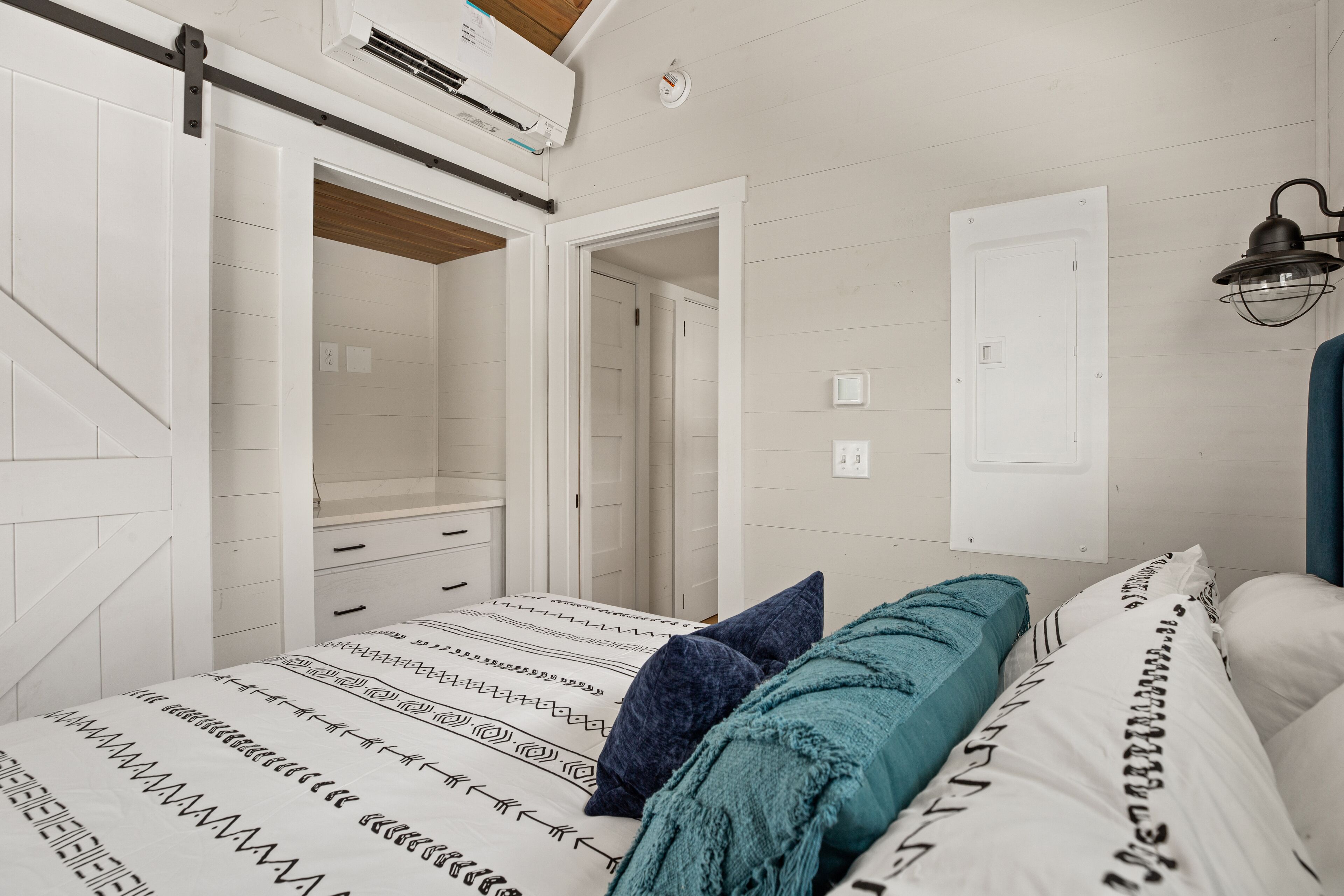 A bedroom with a bed, a nightstand, a dresser, and a door leading to another room.