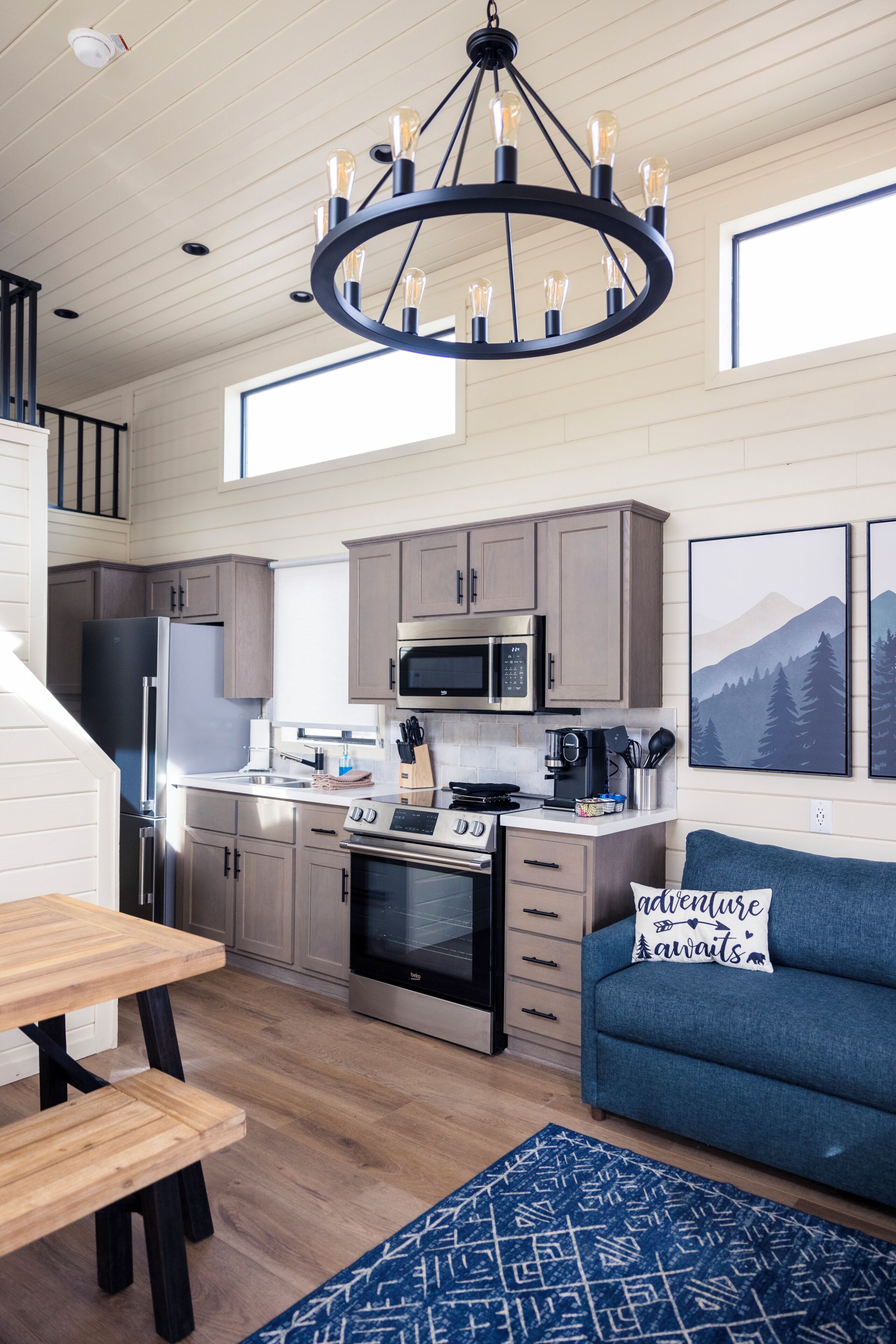 A modern kitchen with stainless steel appliances, a dining area with a wooden table and benches, and a blue sofa with a cushion.