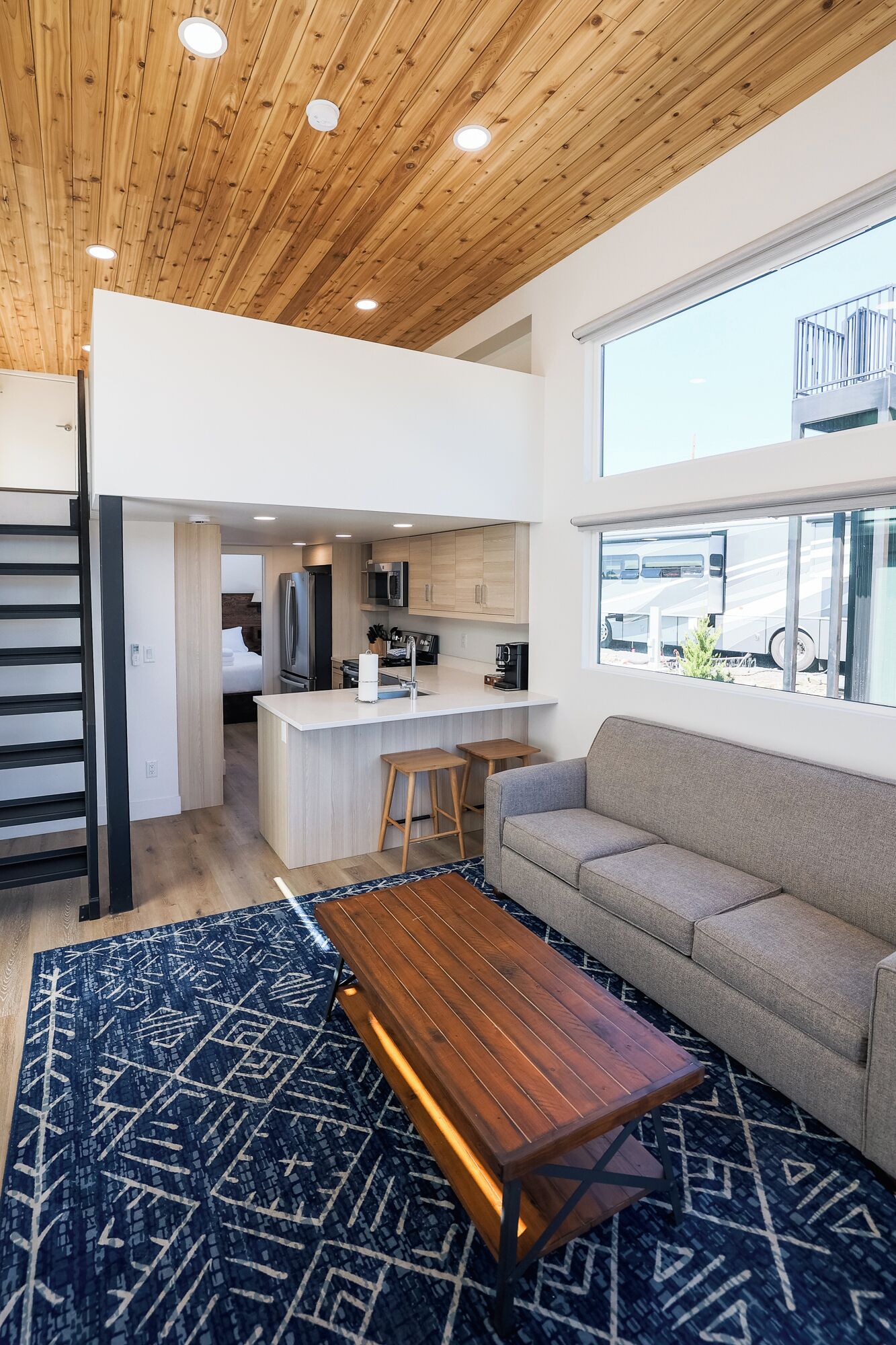 A modern interior with a wooden ceiling, a kitchen area, a sofa, and a patterned rug.