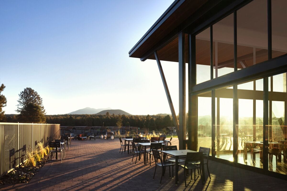 An outdoor dining area with tables and chairs, large windows, and a view of a mountainous landscape.