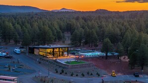 A modern building with a glass facade, surrounded by a forested area, and a parking lot with RVs.