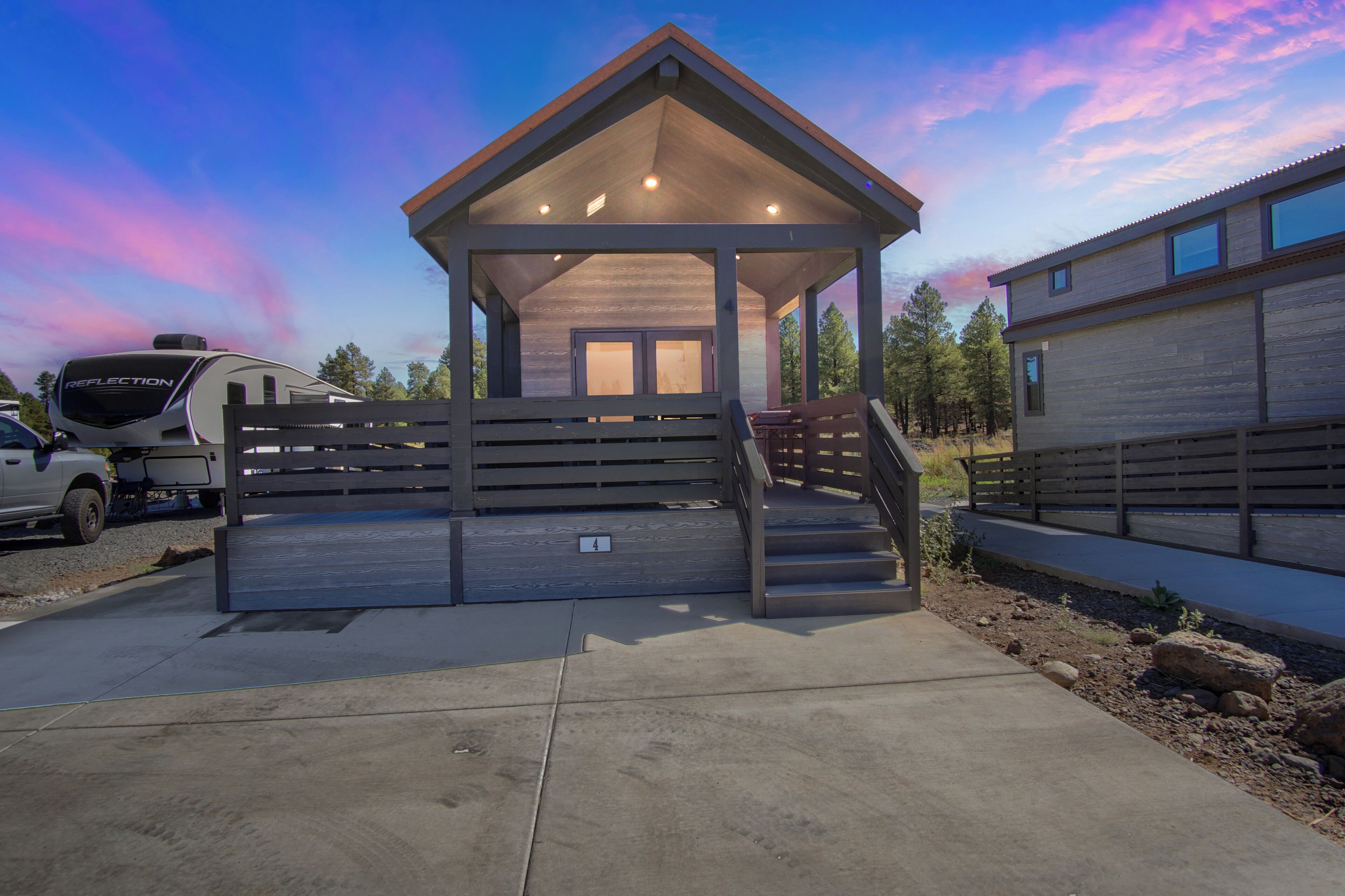A covered outdoor area with a wooden bench, a vehicle, and a building with a sloped roof.