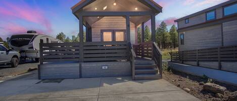 A covered outdoor area with a wooden bench, a vehicle, and a building with a sloped roof.