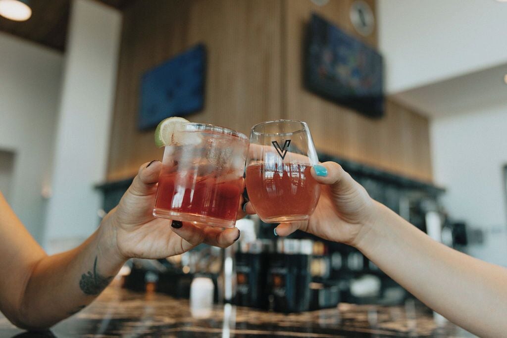 Two hands holding glasses of a red beverage, possibly a cocktail, with a lime wedge on one glass.