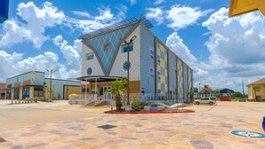 A modern building with a unique geometric facade, a covered entrance, and a paved plaza with a bicycle symbol. - La Vyoma Villas, Westpark Hwy 6 (Houston)