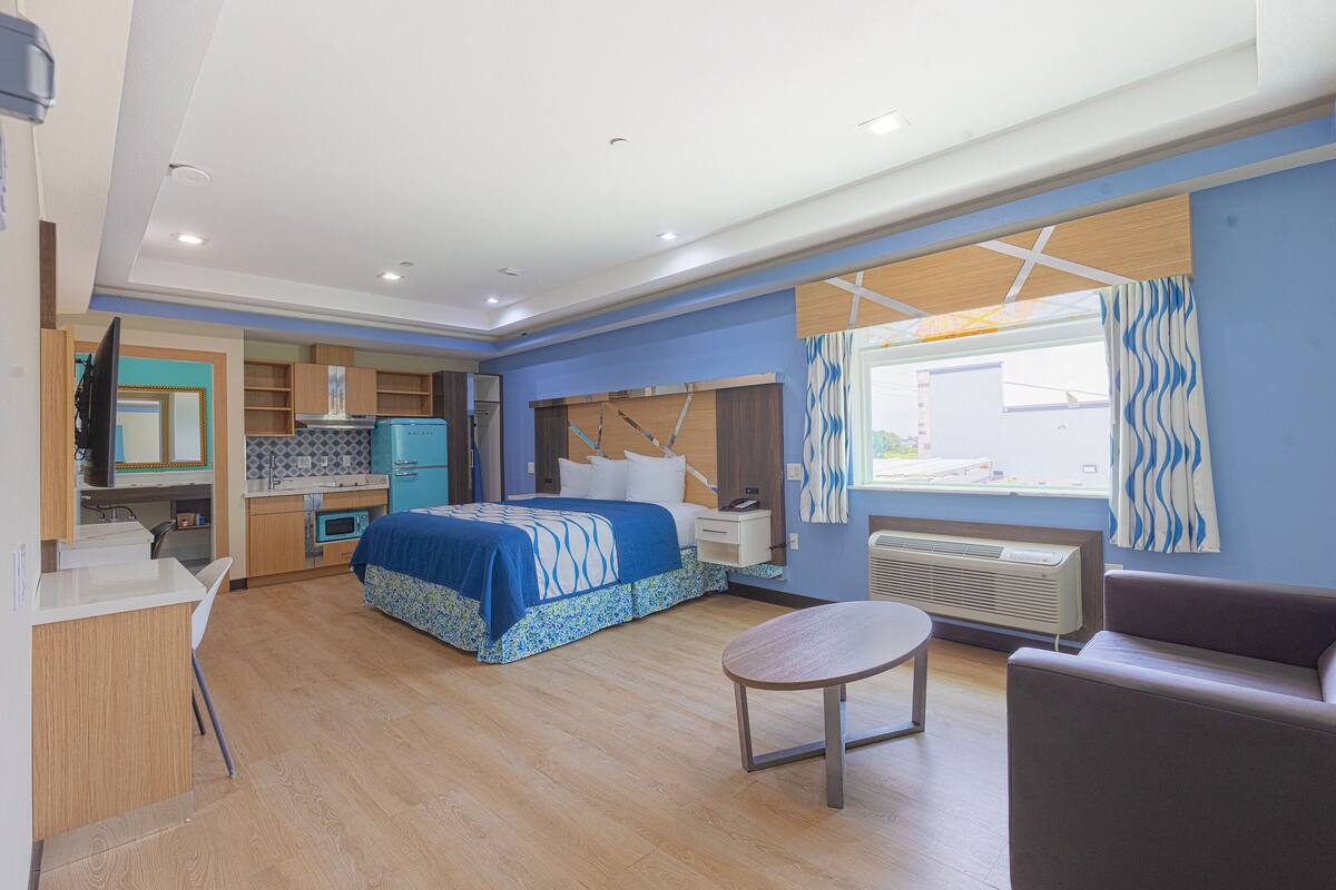 Una camera d'hotel moderna con un letto, una scrivania, una sedia, un divano e una finestra con tende.