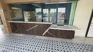 A modern reception desk with a glass partition, a patterned floor, and a view of the outdoors.