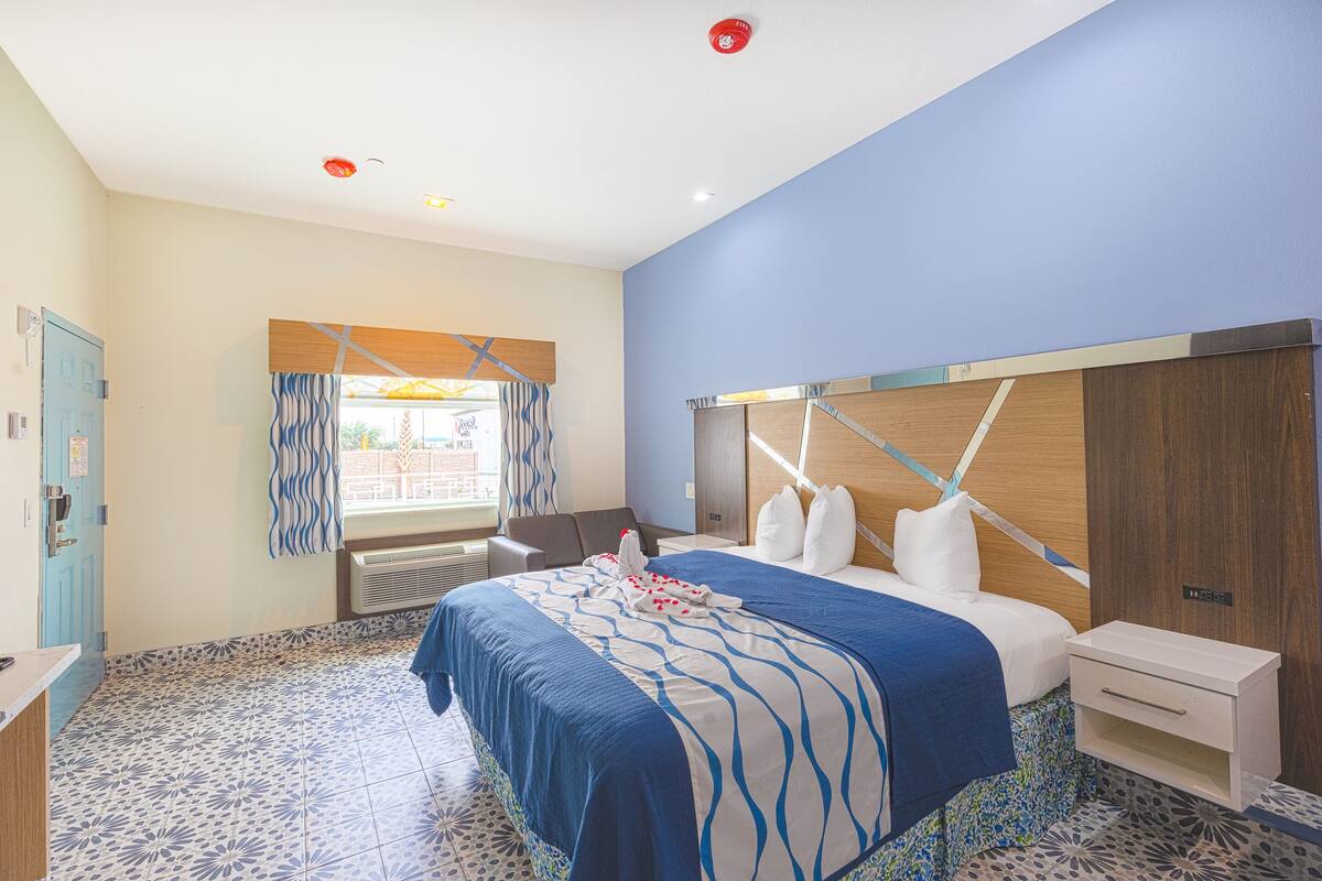 Una camera d'albergo con un letto, una scrivania, una sedia, una finestra con tende e una porta.