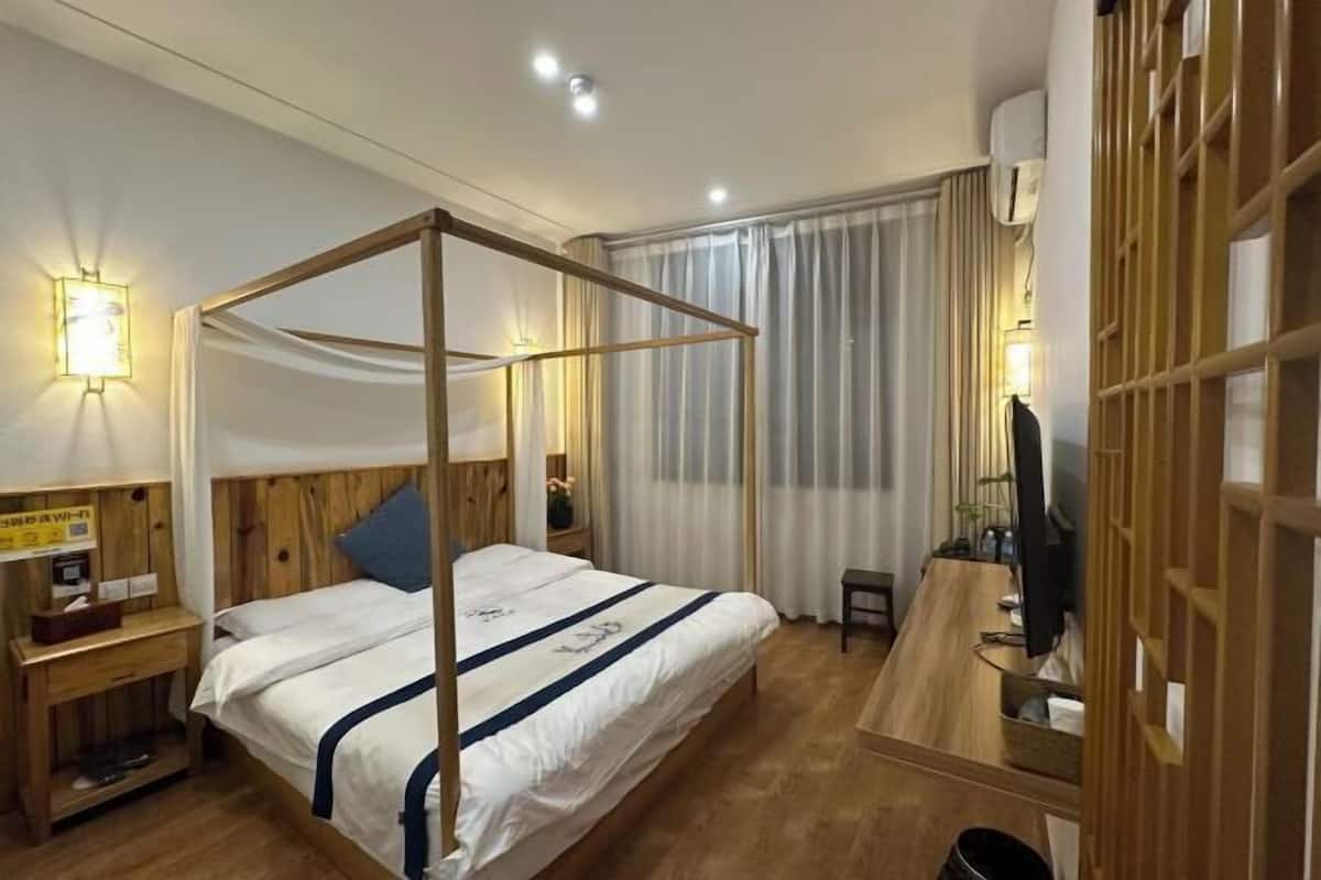 A hotel room with a wooden four-poster bed, a desk with a chair, and a TV.
