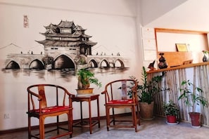 A room with a mural of a traditional bridge, wooden chairs, a small table, and potted plants. - Shijing Homestay (Jianshui Ancient City Branch) (Jianshui)
