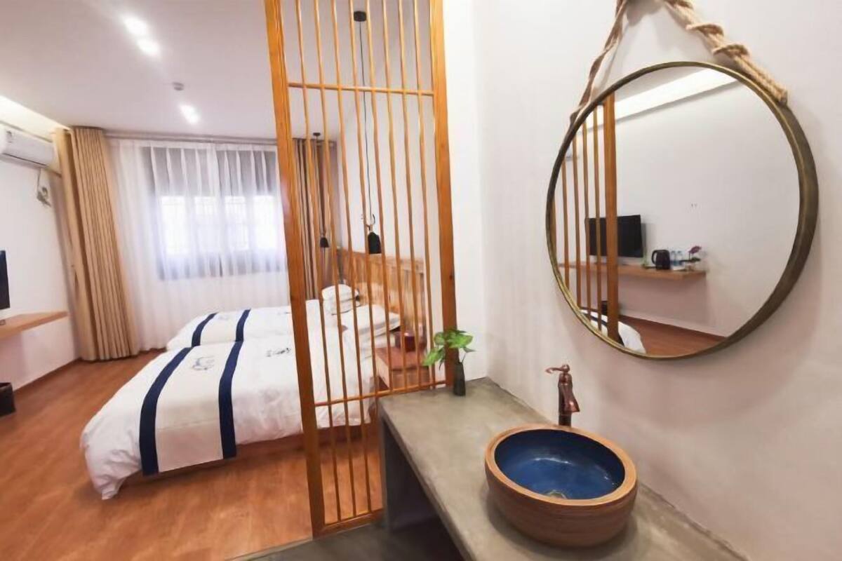 A hotel room with a bed, a wooden partition, a round mirror, and a sink with a blue basin.
