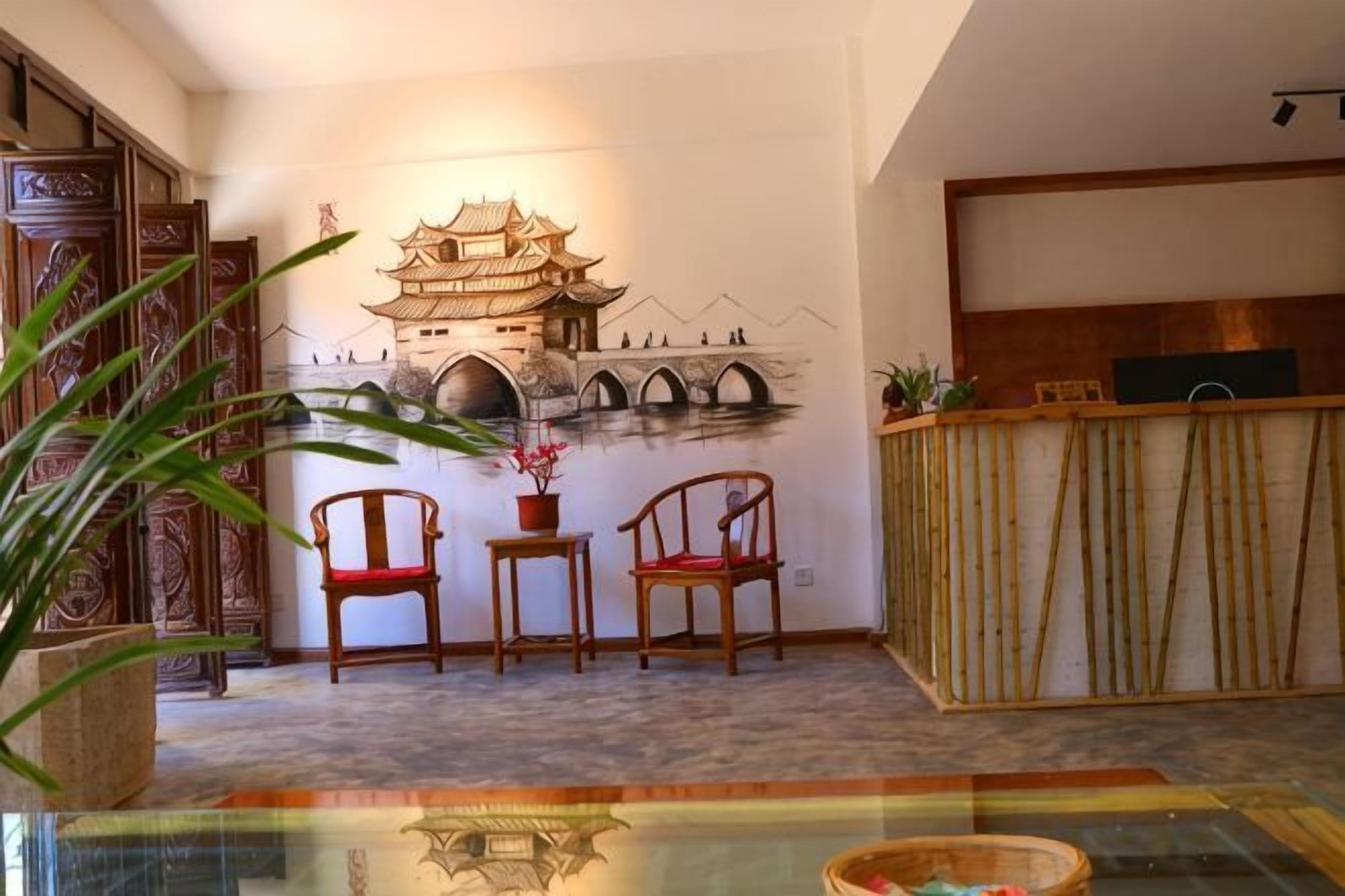 Quarto com mural de arquitetura chinesa tradicional, mobiliário de madeira e mesa de vidro.