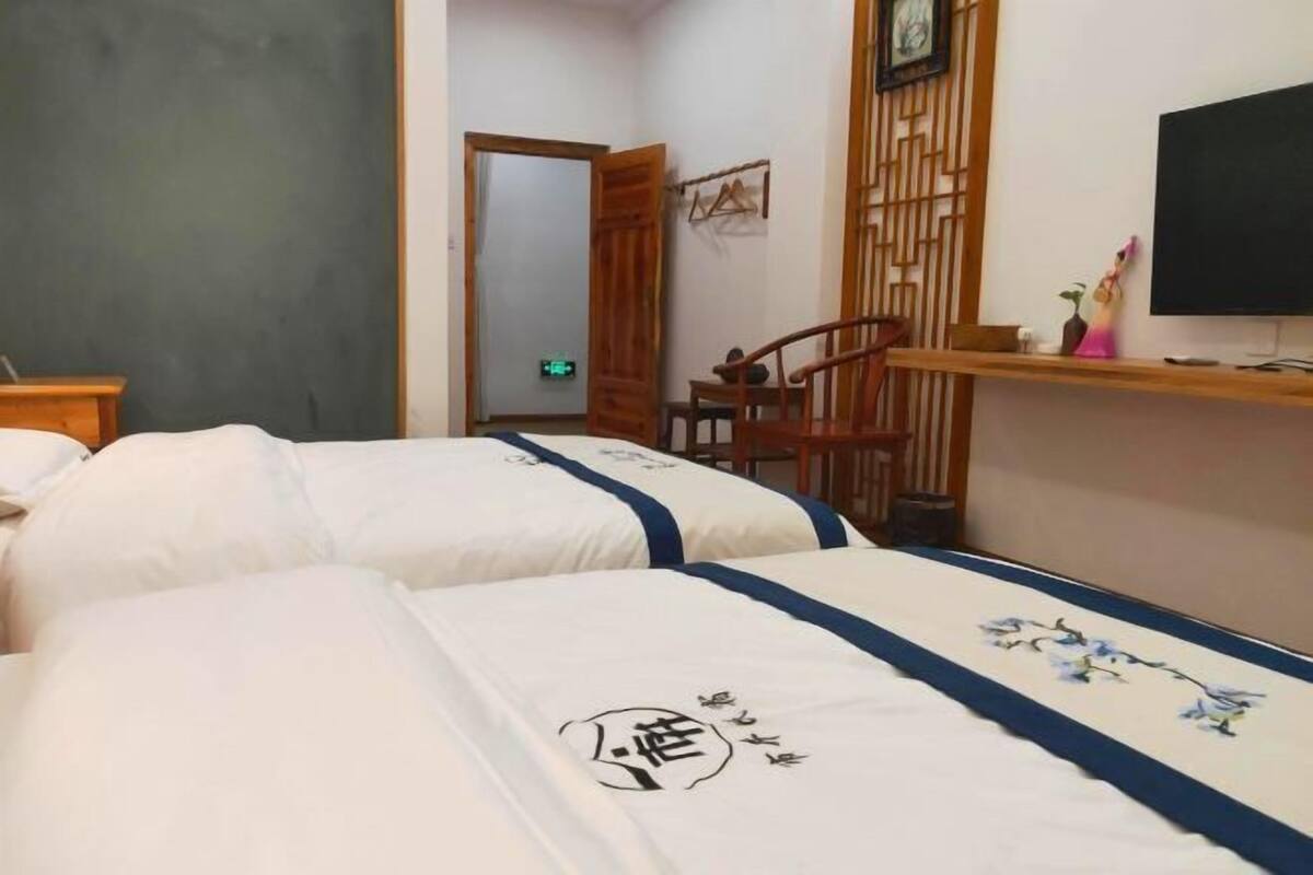 A hotel room with two beds, a wooden chair, a television, and a small shelf with decorative items.