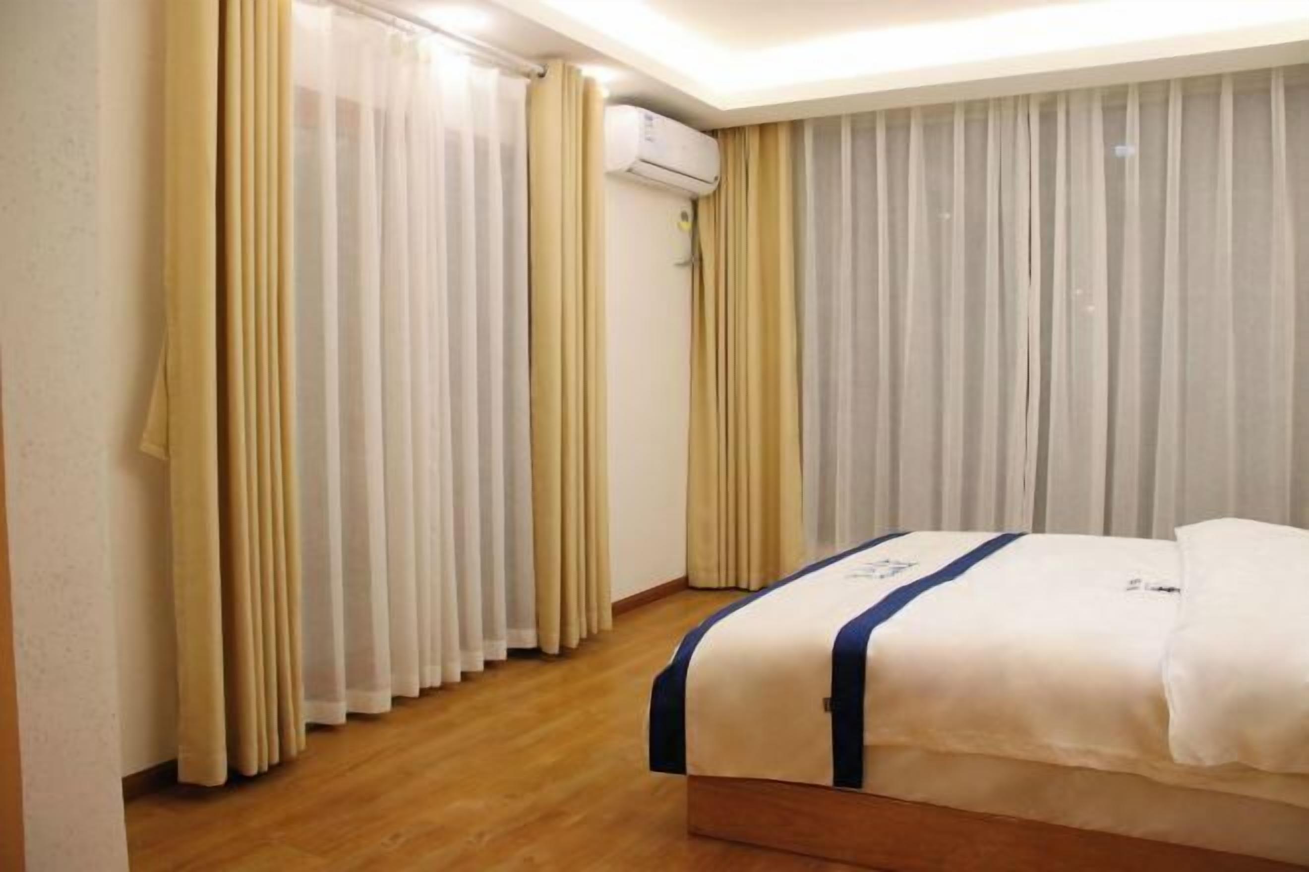 Quarto de hotel com cama, cortinas, ar condicionado e piso de madeira.