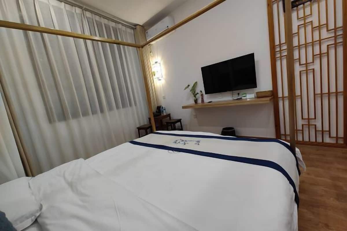 A hotel room with a bed, a TV on a stand, a small table, and a chair.