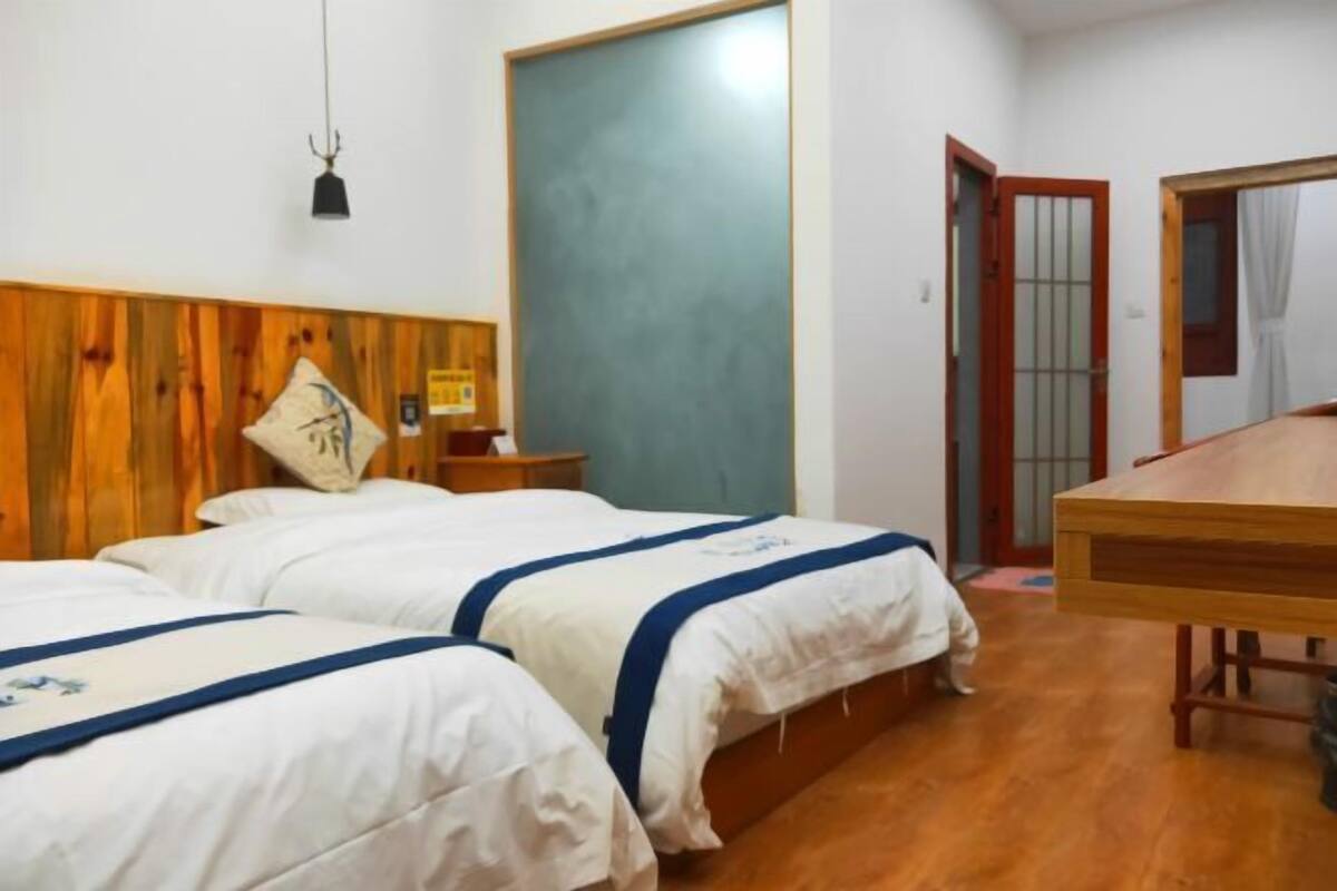 A room with two beds, a wooden headboard, a wooden table, and a door with a frosted glass panel.