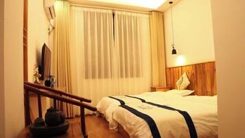 Habitación de hotel con cama, cabecera de madera, mesita de noche, lámpara, ventana con cortinas y una escalera de madera.
