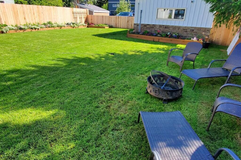 A backyard with a well-maintained lawn, a fire pit, and two lounge chairs.