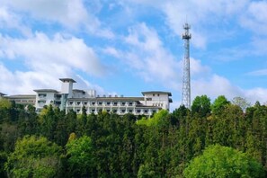 A multi-story building with a prominent communication tower, surrounded by dense green foliage. - Jinshuiwan Holiday Resort (Shucheng)