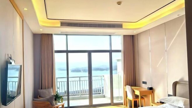 A hotel room with a large window, a bed, a desk, and a chair. - Jinshuiwan Holiday Resort (Shucheng)