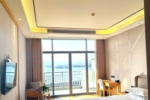 A hotel room with a large window, a bed, a desk, and a chair. - Jinshuiwan Holiday Resort (Shucheng)