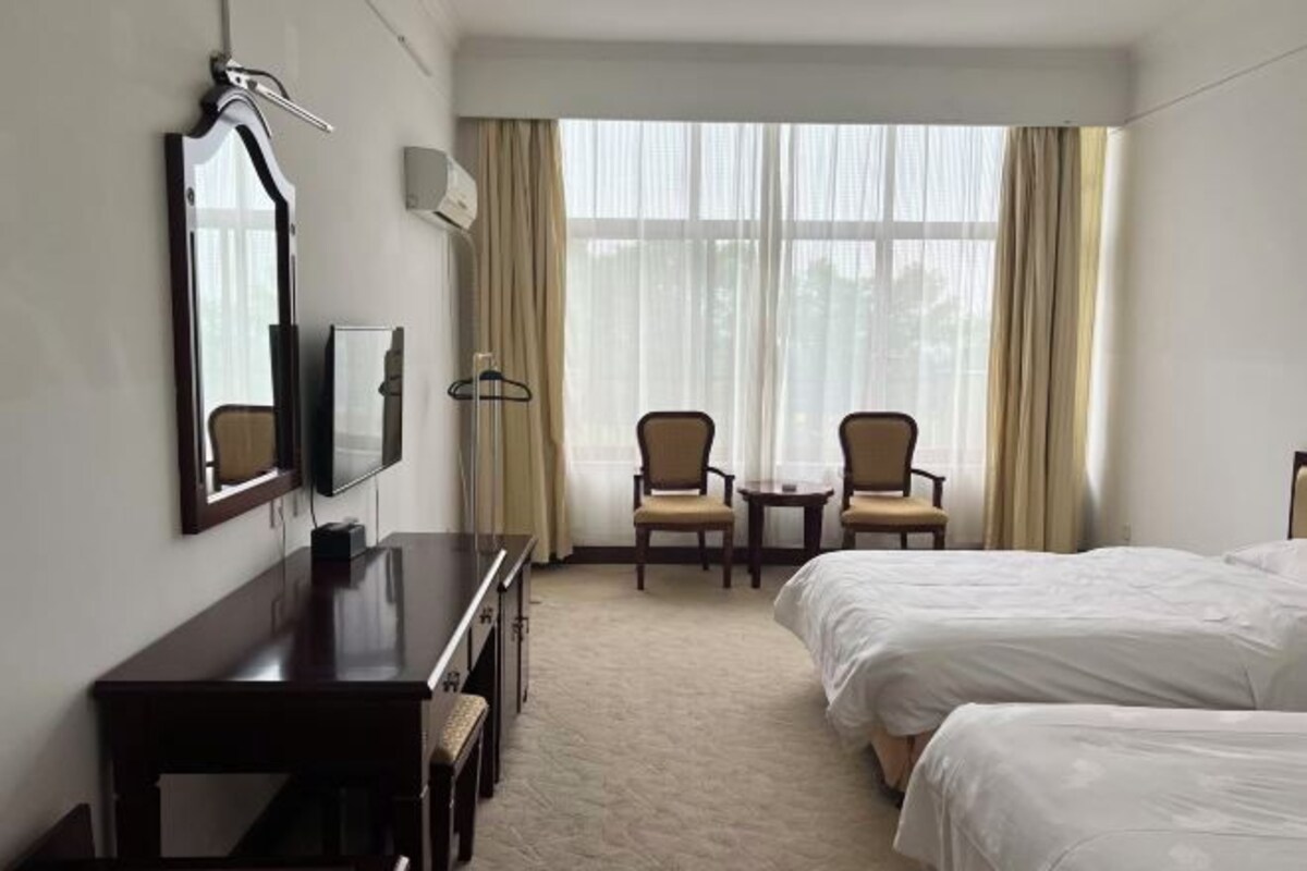 A hotel room with two beds, a desk, a chair, a TV, and a window with curtains.