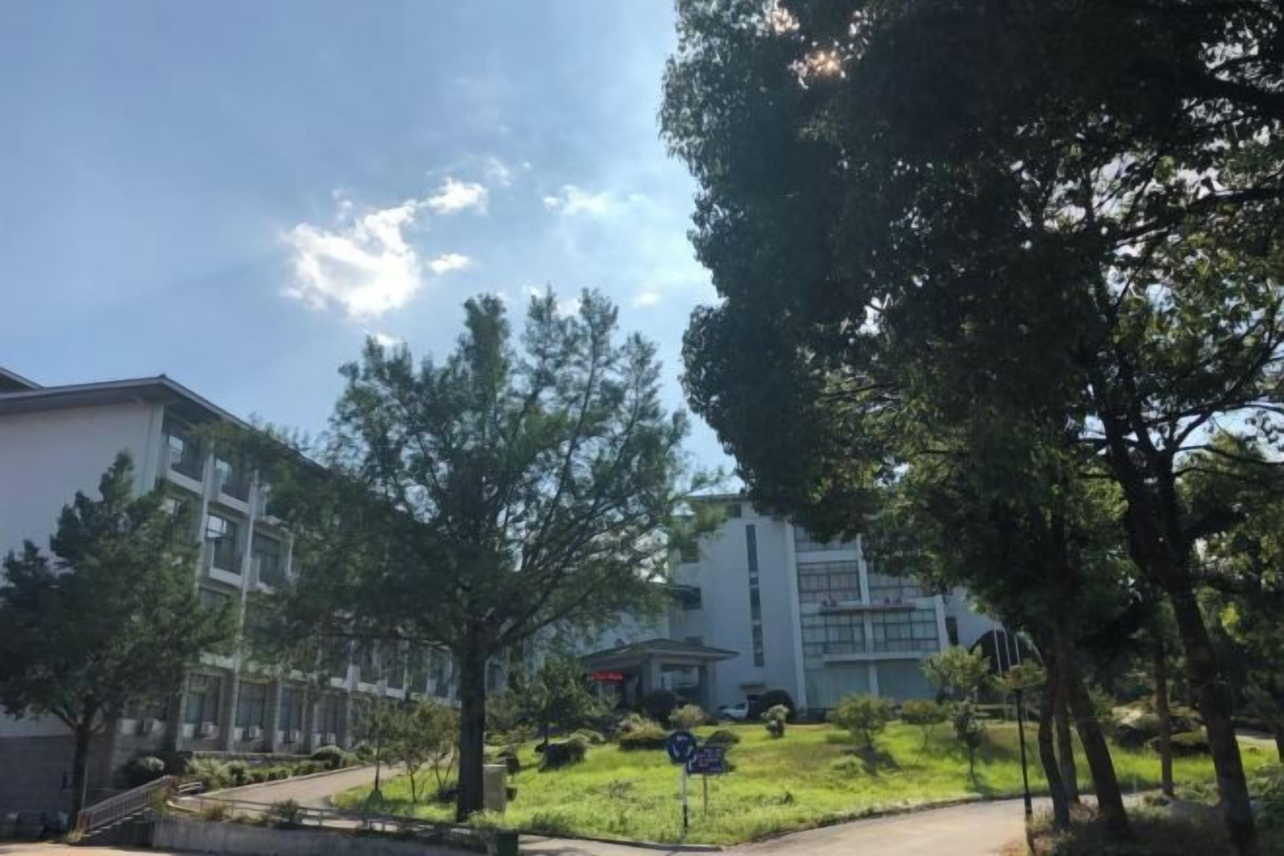 A building with a pathway leading to a parking area, surrounded by trees and greenery.