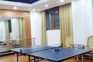 A ping pong table in a room with a mirror, curtains, and wicker chairs. - Jinshuiwan Holiday Resort (Shucheng)