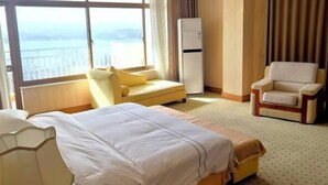 A hotel room with a large bed, a sofa, a chair, and a view of the sea. - Jinshuiwan Holiday Resort (Shucheng)