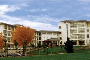 A multi-story building with a flat roof, a central entrance with a canopy, and a parking area with cars. - Jinshuiwan Holiday Resort (Shucheng)