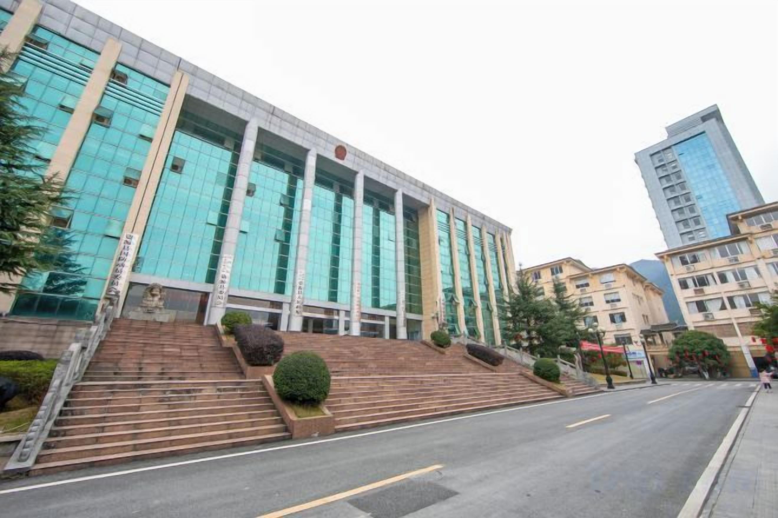 A modern building with a glass facade, a set of stairs leading to the entrance, and a clear sky.