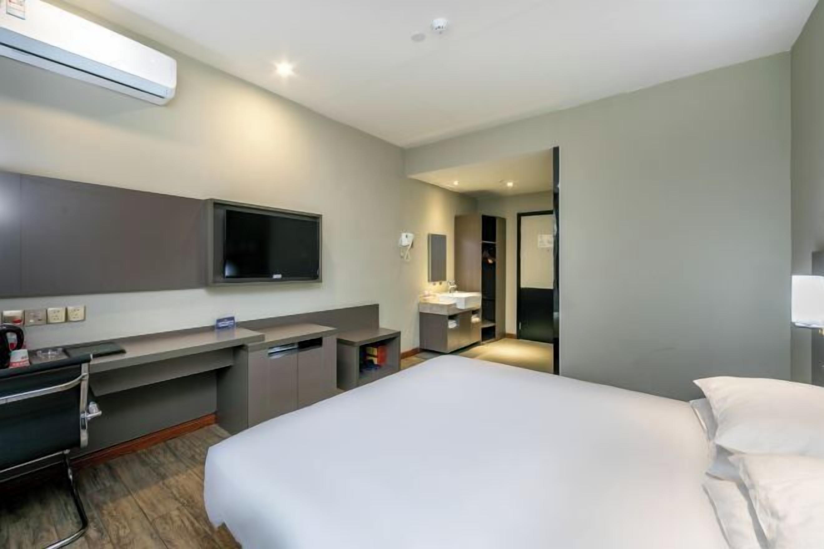 A hotel room with a bed, a desk, a chair, a TV, a mirror, a sink, and a wardrobe.